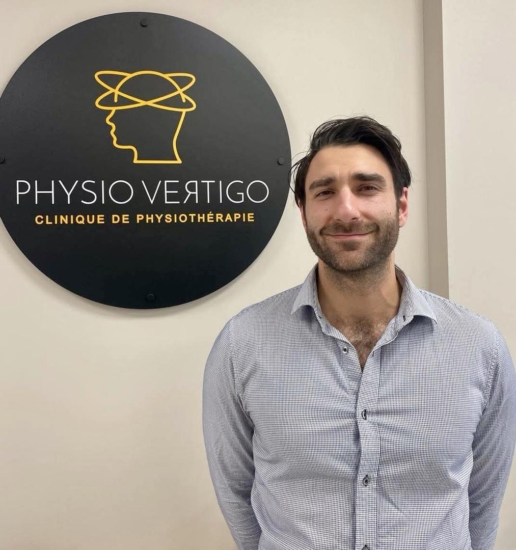 A man standing beside the round gold Physio Vertigo clinic sign